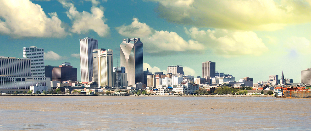 Skyline of New Orleans with various high-rise buildings, viewed from across a wide river under a partly cloudy sky.